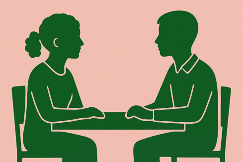 Two people sitting at a table, facing each other, engaged in conversation.